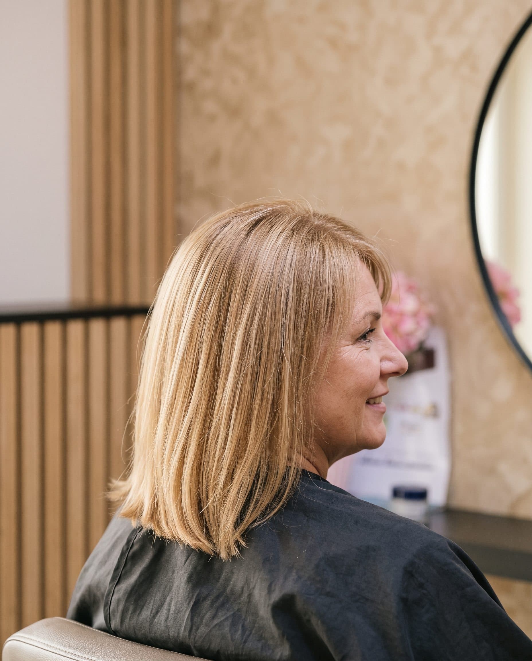 Klant met vers geknipt halflang blond haar bij de ronde spiegel in de salon