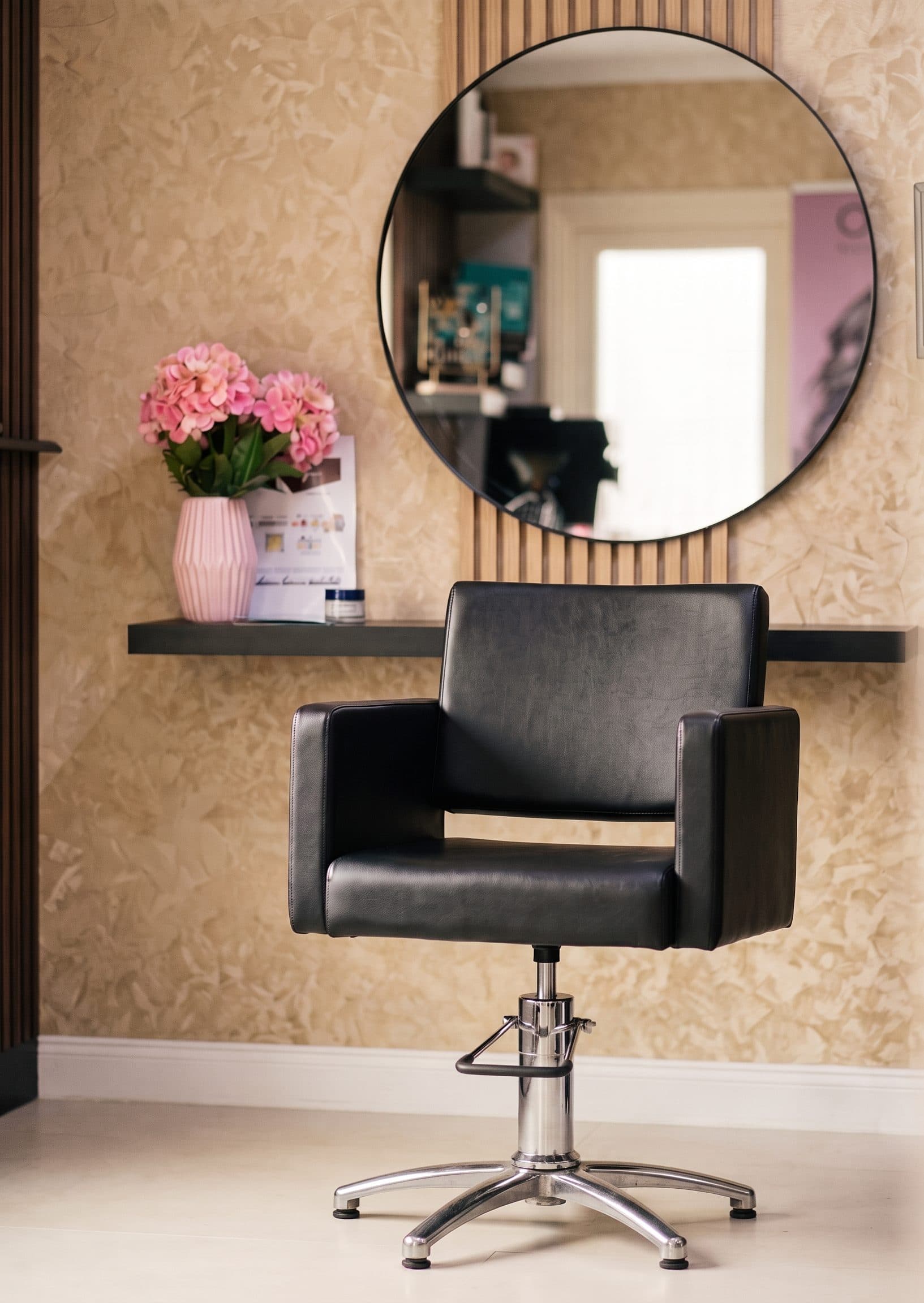 De salon met een kappersstoel, een ronde spiegel en roze bloemen